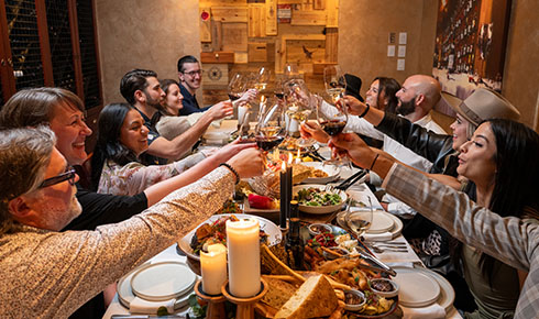 Personen sitzen an einem Tisch mit viel schön angerichtetem Essen und stoßen miteinander an