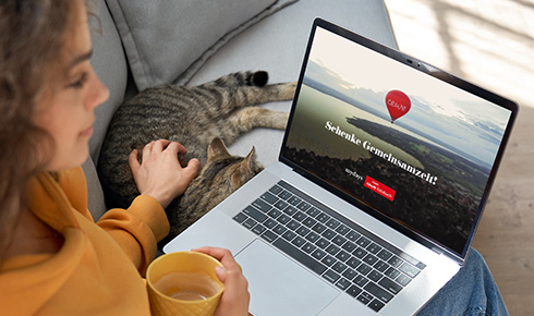 Frau sitzt auf Sofa und schaut auf ihrem Laptop den Werbespot von Cewe und mydays