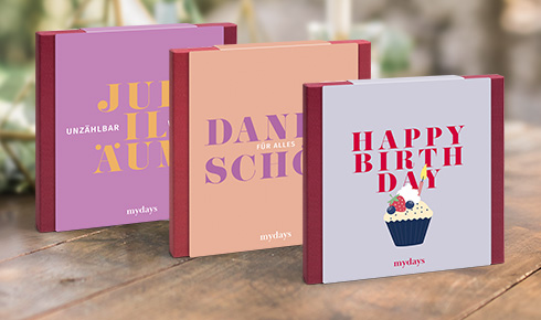 Die drei mydays-Geschenkboxen "Jubiläum", "Dankeschön" und "Happy Birthday" stehen aufgereit auf einem Tisch mit festlichem Hintergrund.